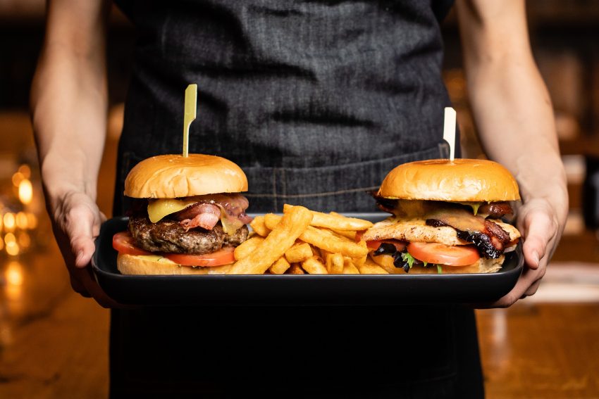 closeup of person holding tray at waist with 2 burgers and fries