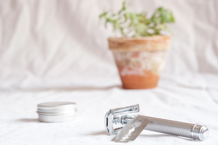 shaving razor on a white surface, potted plant in background