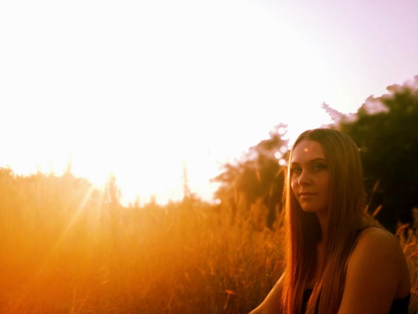 woman sits outside in grass, tree behind, lens flare from sunlight