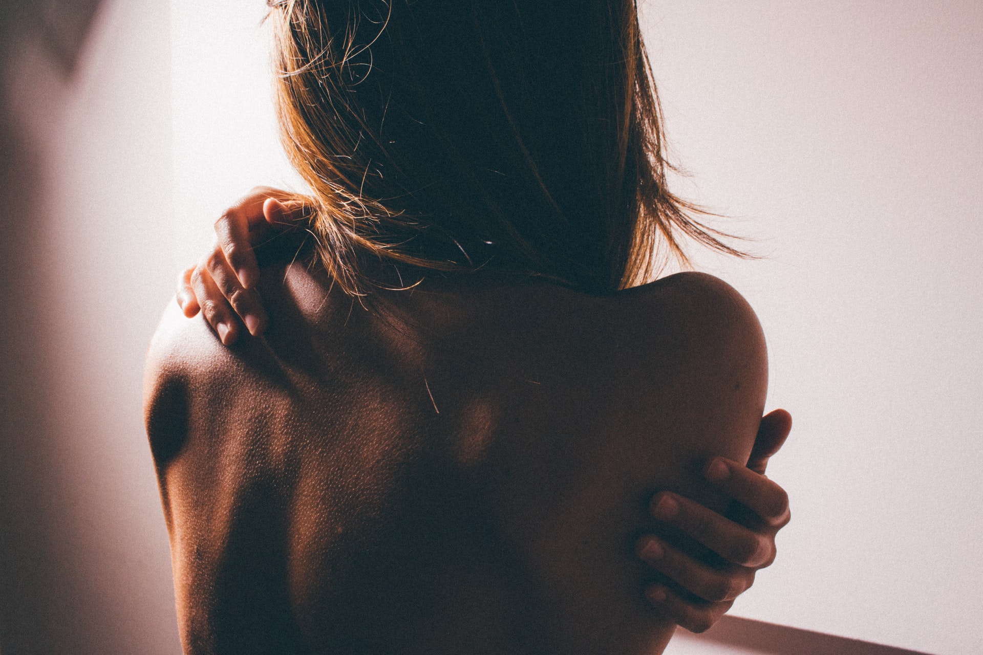 topless person facing away from the camera, hands reaching round her back, itchy skin, eczema awareness