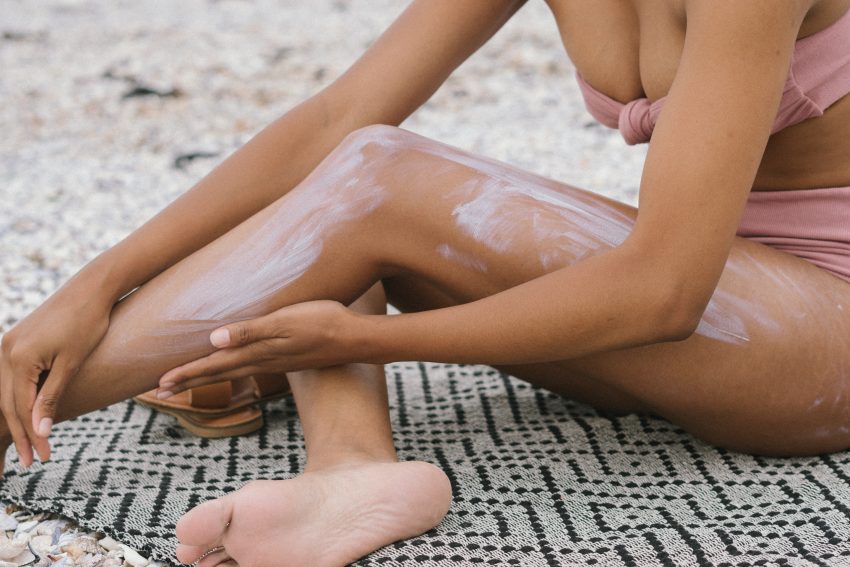woman in bathing suit applying cream to leg