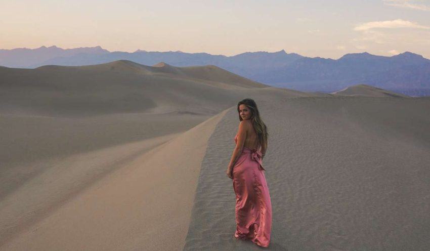 Person in light dress stands in a hot desert, looking over shoulder at camera