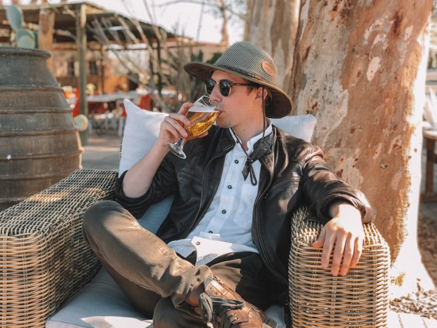 person sitting in wicker chair drinking beer in the sun, how alcohol affects our skin
