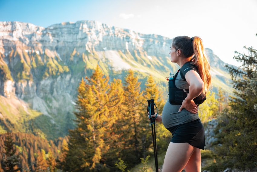 pregnant woman on a hike, looks past trees to mountain scenery
