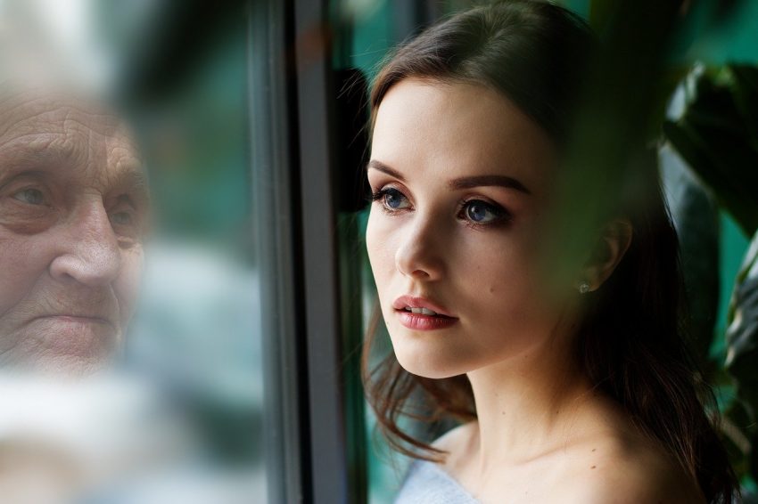 pensive young woman looks in reflection of an old woman
