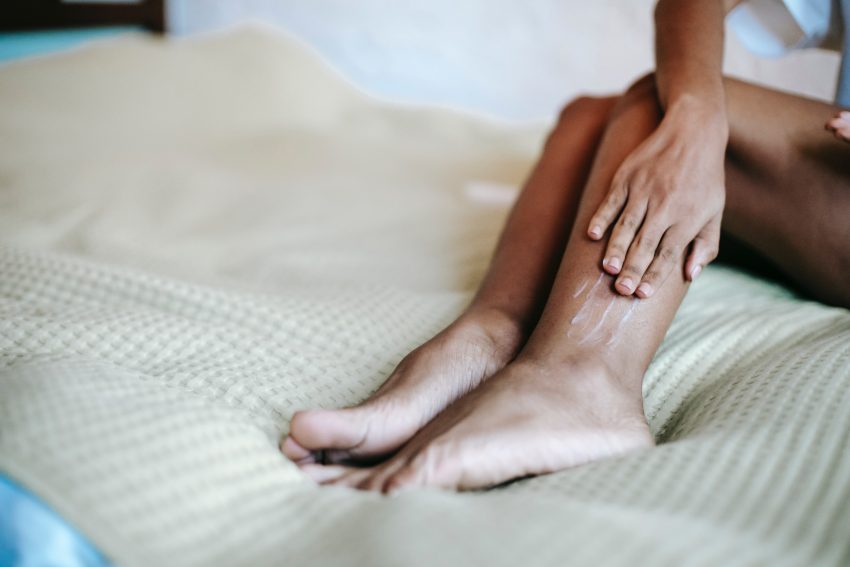 person applying moisturiser to leg skin, sitting on soft surface