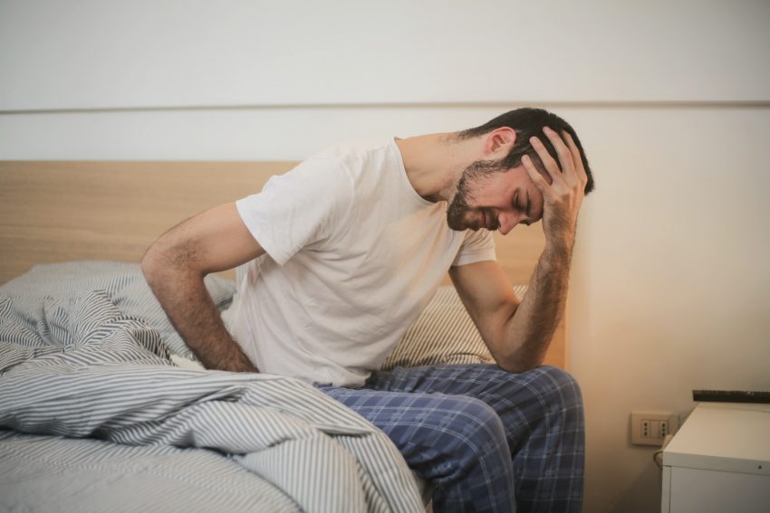 side effects of alcohol, man with hangover sits on edge of bed, head in hand