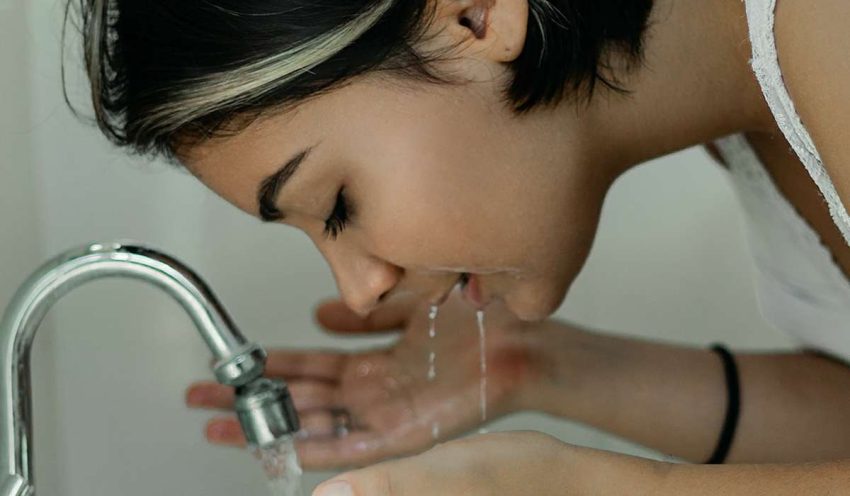 person washing face at sink, water dripping from her mouth