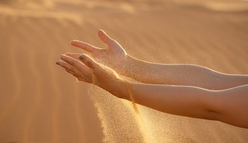 person's hands releasing sand, sandy background, summer skincare tips
