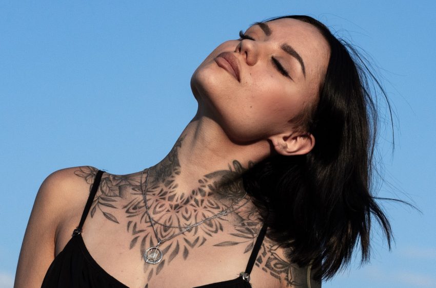 person with tattoos and eyes closed faces the sun