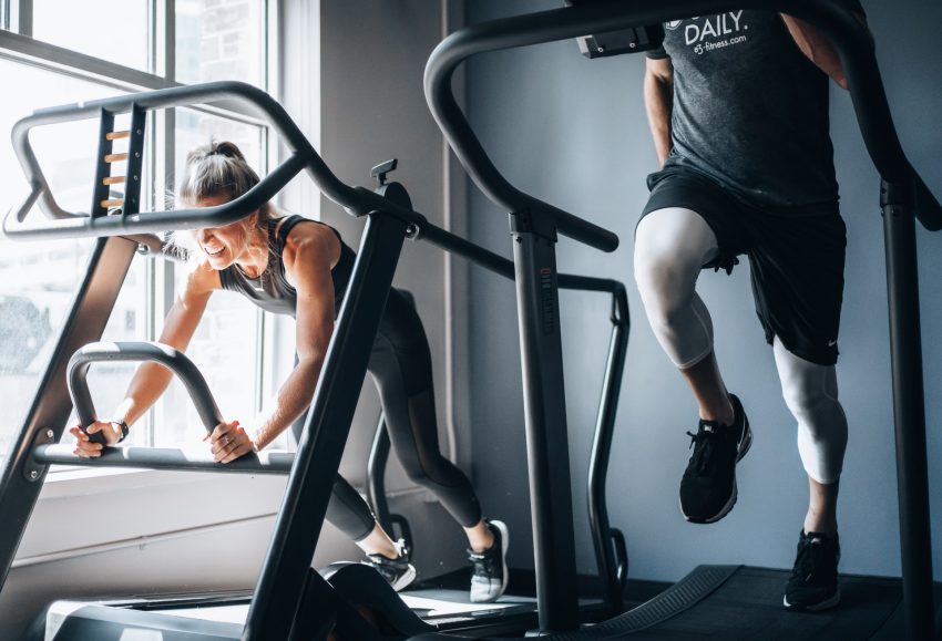 Two people exercising on treadmills inside, next to a window