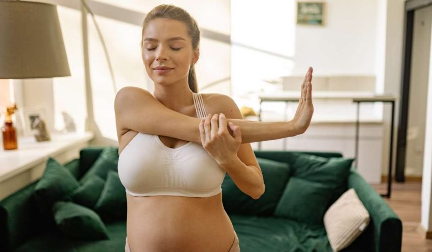 Person with a mum tum stretching one arm across body, exercising to reduce mum tum